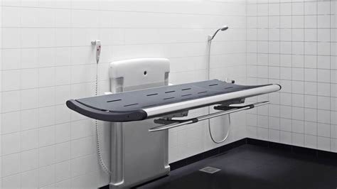 Adult changing table - The SCT 3000 series has a stylish and award-winning design focused on comfort and ease of use. SCT 3000 shower change table, powered, height adjustable 700 mm; from 300 mm -1000 mm, with wired hand control. Foldable. Incl. safety rail, flexible hose (Ø32 mm) and water collection tray with integrated outlet.